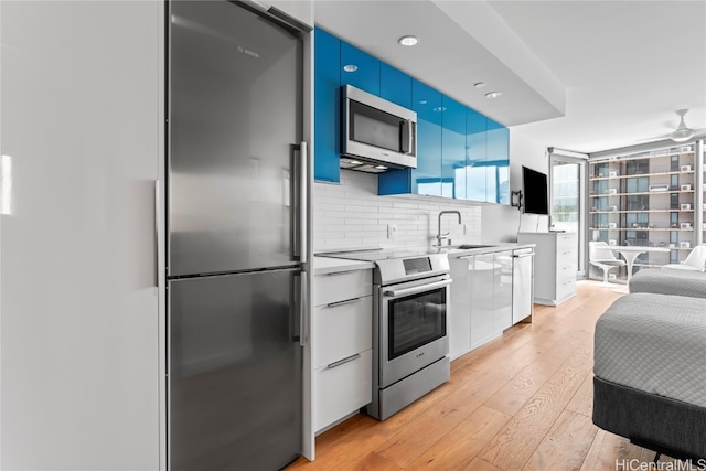 kitchen featuring backsplash, blue cabinets, sink, light hardwood / wood-style floors, and stainless steel appliances