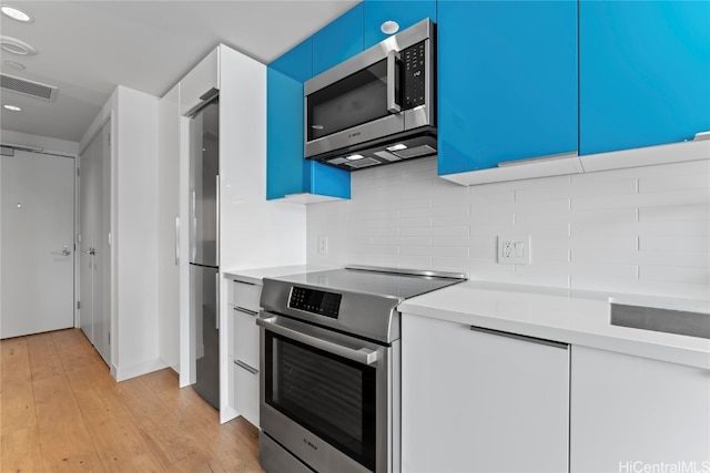 kitchen with tasteful backsplash, white cabinets, stainless steel appliances, and light wood-type flooring