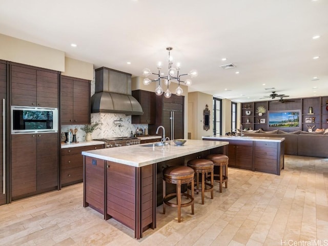 kitchen with dark brown cabinets, custom range hood, and a large island with sink