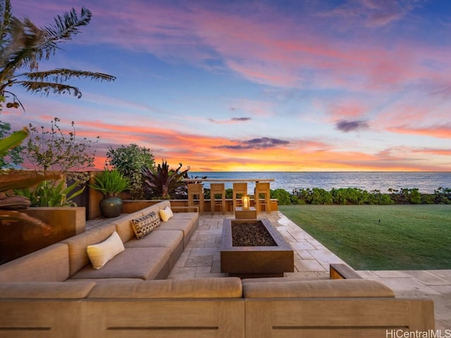 patio terrace at dusk featuring a lawn, an outdoor living space with a fire pit, and a water view