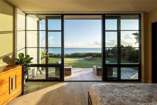 bedroom with wood-type flooring, a water view, and expansive windows