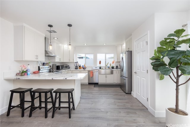 kitchen with kitchen peninsula, appliances with stainless steel finishes, light wood-type flooring, a kitchen bar, and white cabinets