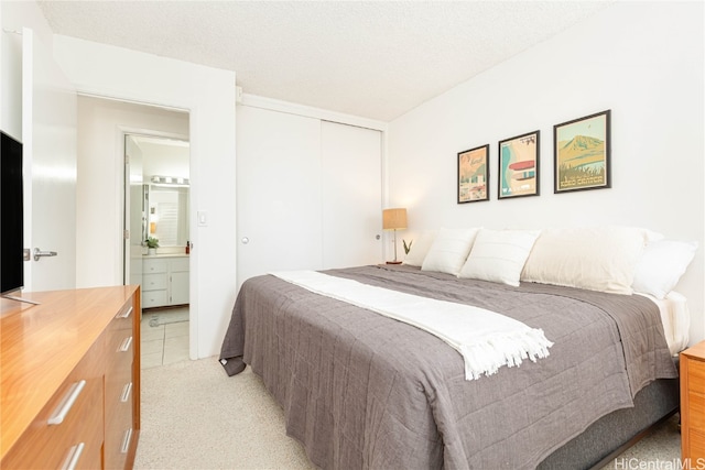 bedroom with a textured ceiling, light carpet, ensuite bathroom, and a closet