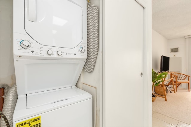 laundry area with stacked washer / dryer, a textured ceiling, and light tile patterned floors