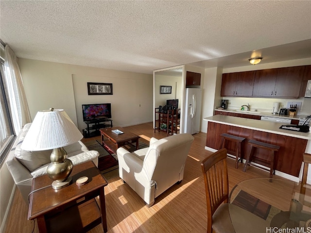 living room with a textured ceiling, sink, and light wood-type flooring