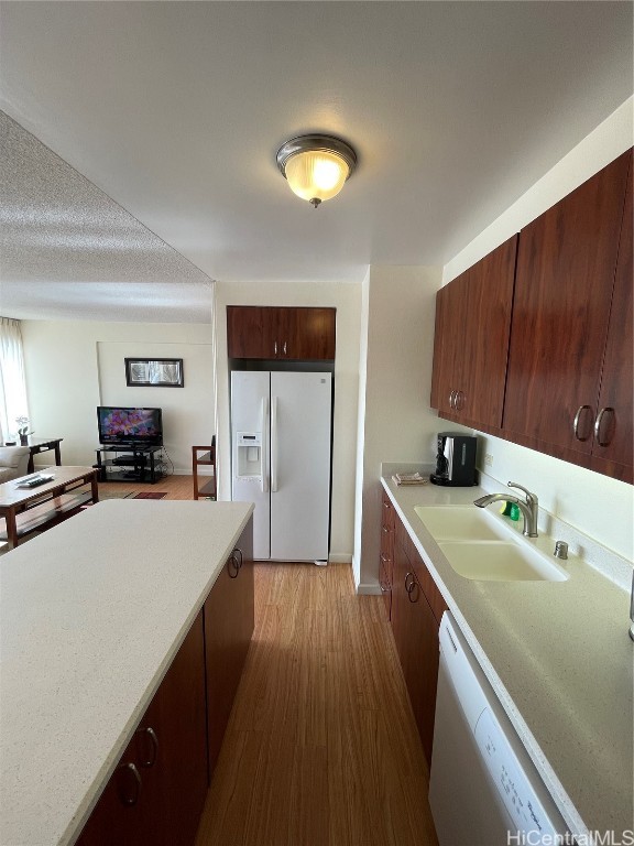 kitchen with sink, light hardwood / wood-style floors, a textured ceiling, and white appliances