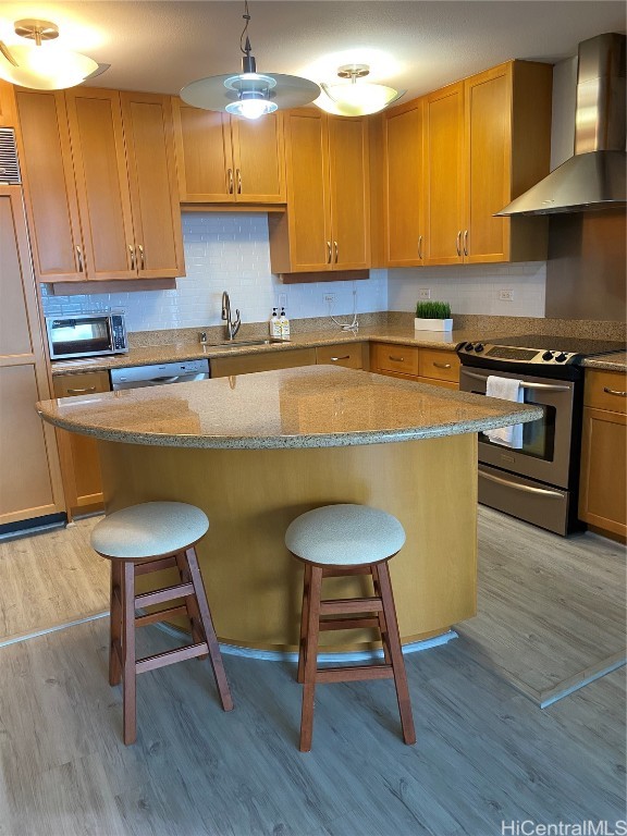 kitchen with wall chimney range hood, a breakfast bar, stainless steel appliances, and light hardwood / wood-style floors