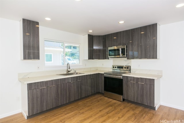 kitchen with appliances with stainless steel finishes, sink, dark brown cabinets, and light hardwood / wood-style floors