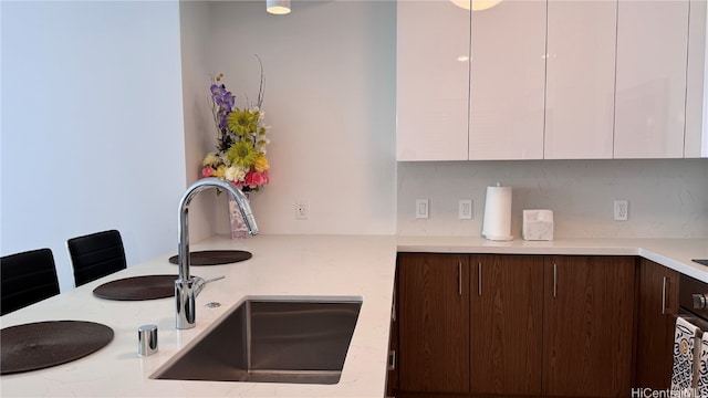 kitchen with decorative backsplash, white cabinets, dark brown cabinetry, and sink