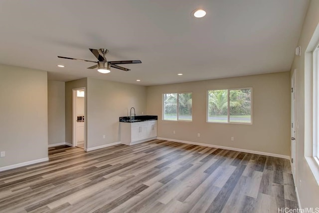 unfurnished living room with light hardwood / wood-style floors, sink, and ceiling fan