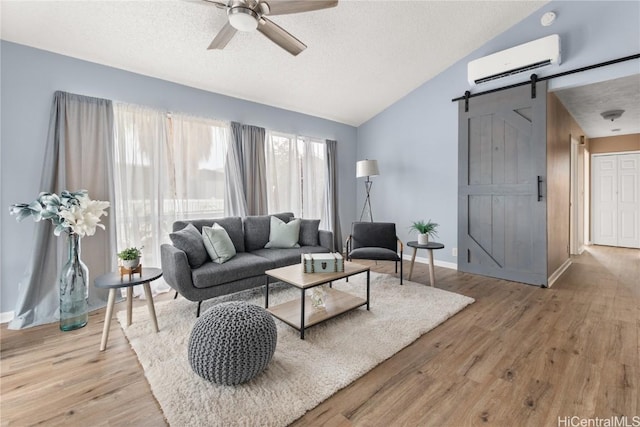 living room featuring a barn door, vaulted ceiling, a textured ceiling, an AC wall unit, and light wood-style floors