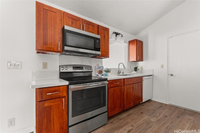 kitchen featuring sink, hardwood / wood-style floors, a textured ceiling, lofted ceiling, and appliances with stainless steel finishes