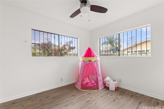 rec room with a ceiling fan, baseboards, and wood finished floors