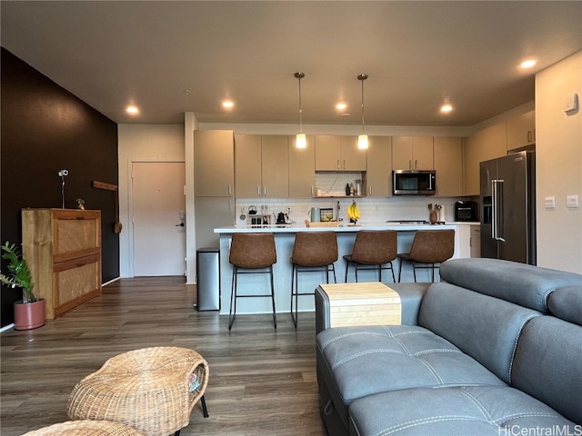 kitchen featuring tasteful backsplash, appliances with stainless steel finishes, a kitchen breakfast bar, decorative light fixtures, and dark wood-type flooring