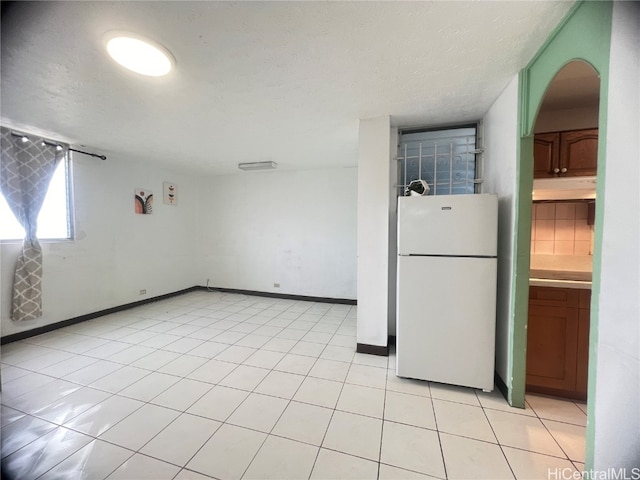 kitchen with light tile patterned flooring, white fridge, a textured ceiling, and tasteful backsplash