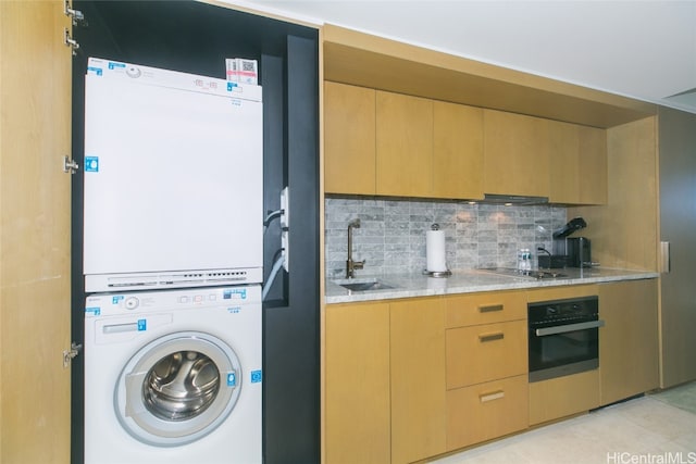 kitchen with stacked washer and clothes dryer, oven, backsplash, sink, and light stone counters