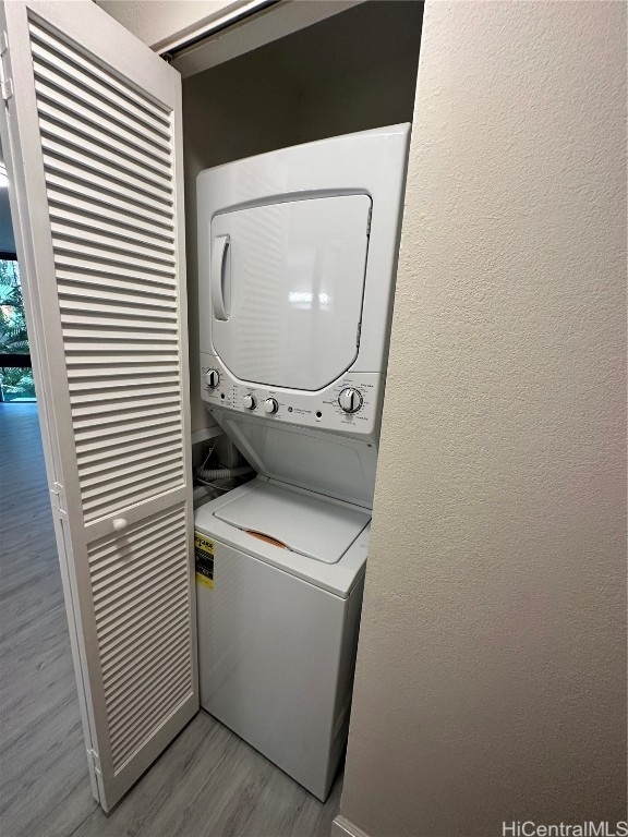 washroom with stacked washer / drying machine and light hardwood / wood-style flooring