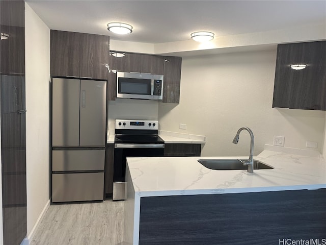 kitchen with kitchen peninsula, dark brown cabinets, appliances with stainless steel finishes, light wood-type flooring, and sink