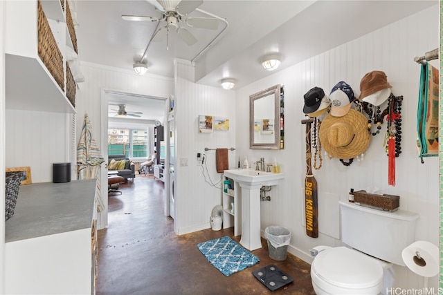 bathroom with wood walls, toilet, concrete floors, and ceiling fan