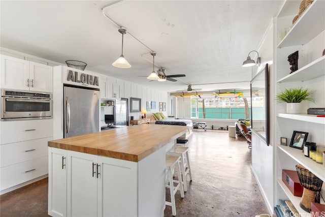 kitchen with appliances with stainless steel finishes, concrete floors, white cabinetry, and wooden counters