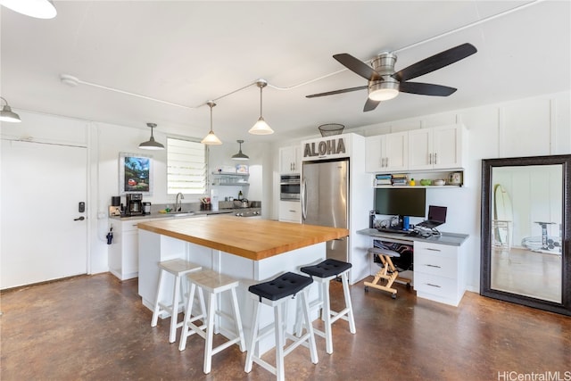 kitchen featuring white cabinetry, butcher block countertops, stainless steel appliances, and a center island