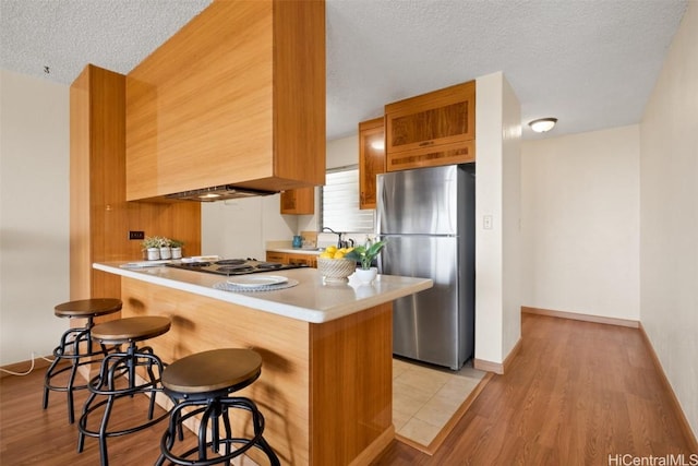 kitchen featuring a kitchen breakfast bar, kitchen peninsula, stainless steel appliances, a textured ceiling, and light hardwood / wood-style flooring