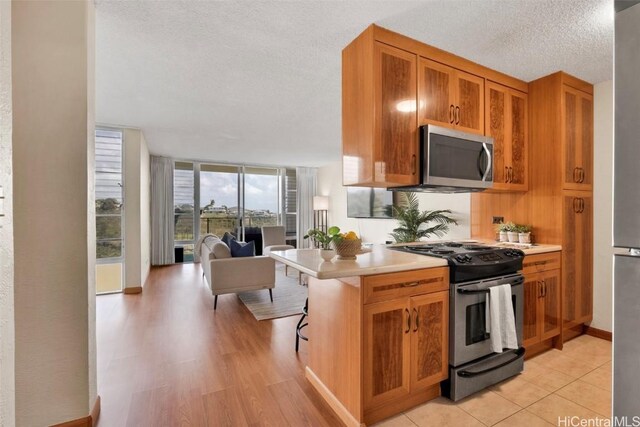 kitchen featuring appliances with stainless steel finishes, a kitchen breakfast bar, expansive windows, kitchen peninsula, and a textured ceiling