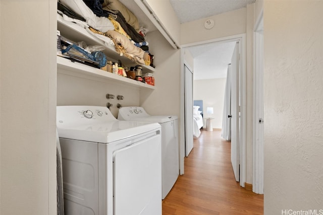 laundry room with light hardwood / wood-style flooring, washer and clothes dryer, and a textured ceiling