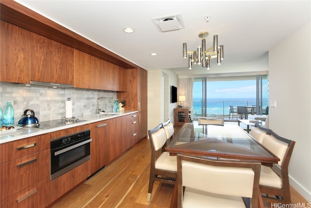 kitchen featuring decorative backsplash, stainless steel oven, light hardwood / wood-style flooring, a notable chandelier, and sink