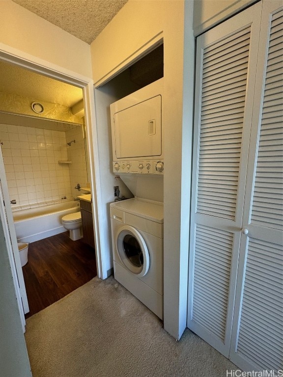 laundry room with a textured ceiling, stacked washer and dryer, and light hardwood / wood-style flooring