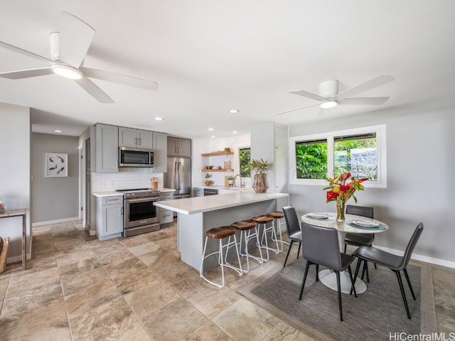 kitchen featuring appliances with stainless steel finishes, sink, backsplash, gray cabinetry, and a breakfast bar