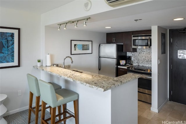 kitchen with kitchen peninsula, a kitchen bar, tasteful backsplash, dark brown cabinets, and stainless steel appliances