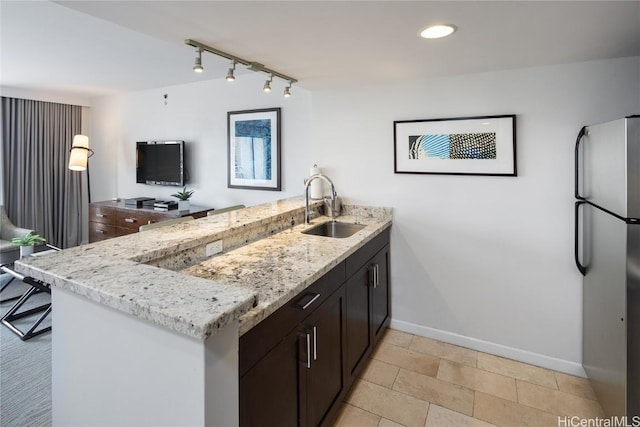 kitchen with sink, stainless steel fridge, light stone countertops, dark brown cabinets, and kitchen peninsula