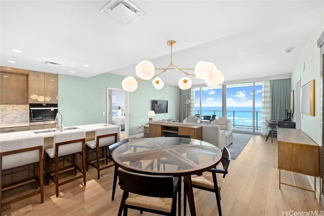 dining room featuring floor to ceiling windows, sink, a notable chandelier, and light hardwood / wood-style flooring