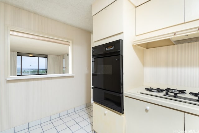 kitchen featuring white cabinets, light tile patterned floors, white gas stovetop, a textured ceiling, and double oven