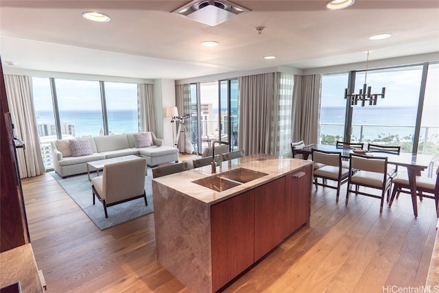 kitchen with sink, a water view, light hardwood / wood-style flooring, a chandelier, and a center island with sink