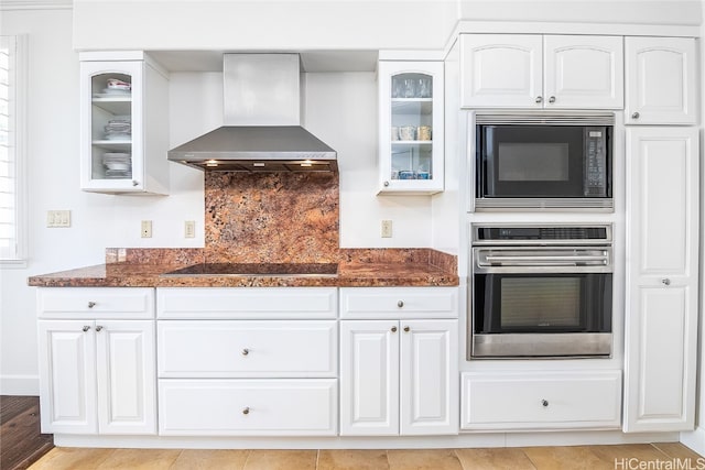 kitchen with black appliances, white cabinetry, wall chimney range hood, and dark stone countertops