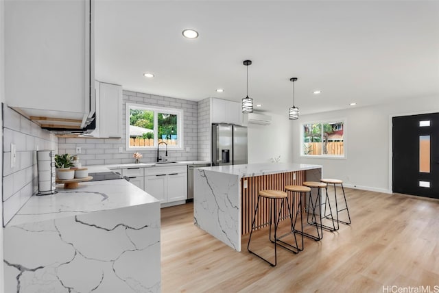 kitchen with a wall mounted AC, appliances with stainless steel finishes, white cabinetry, decorative light fixtures, and a center island