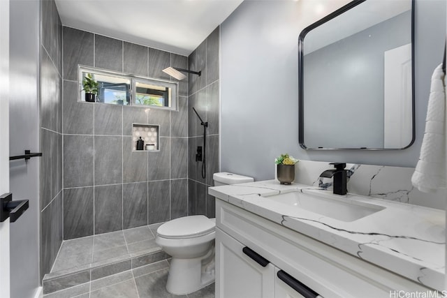 bathroom with vanity, toilet, a tile shower, and tile patterned flooring