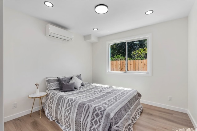 bedroom with light hardwood / wood-style floors and an AC wall unit