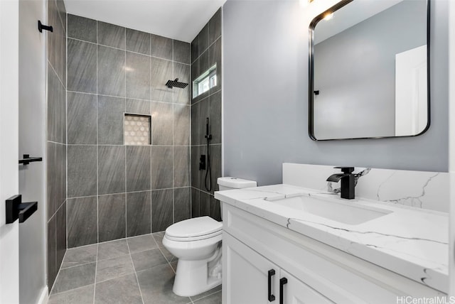 bathroom with vanity, toilet, a tile shower, and tile patterned flooring