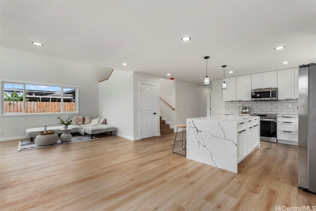 kitchen featuring light hardwood / wood-style flooring, a center island, pendant lighting, white cabinetry, and appliances with stainless steel finishes