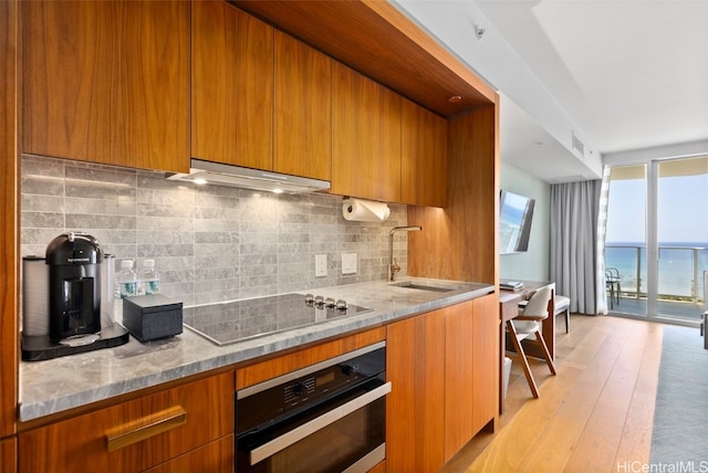 kitchen featuring stainless steel oven, ventilation hood, sink, electric cooktop, and light wood-type flooring