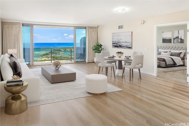 living room featuring a wall of windows, a water view, and light wood-type flooring