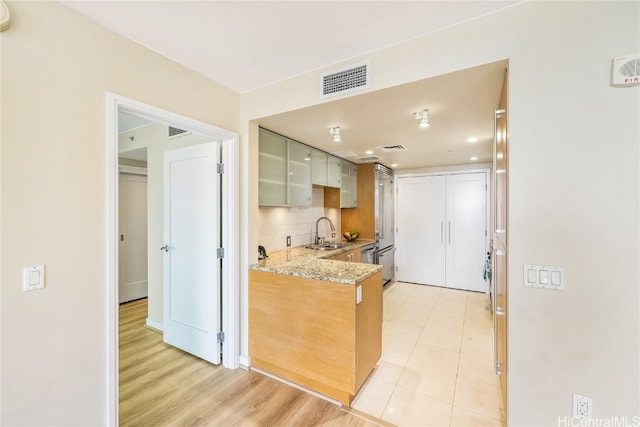 kitchen with light stone countertops, sink, backsplash, kitchen peninsula, and light hardwood / wood-style floors