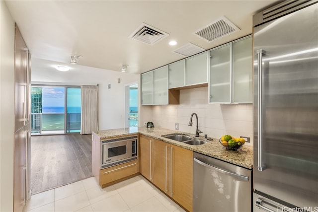 kitchen featuring kitchen peninsula, backsplash, light hardwood / wood-style flooring, built in appliances, and sink