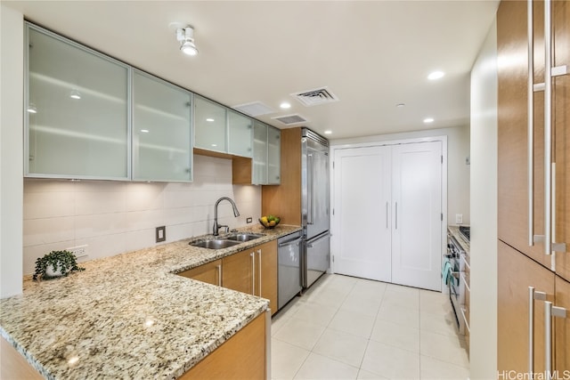 kitchen featuring appliances with stainless steel finishes, sink, light stone countertops, and kitchen peninsula