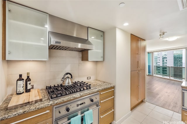 kitchen featuring light stone counters, stainless steel appliances, wall chimney range hood, and light hardwood / wood-style flooring