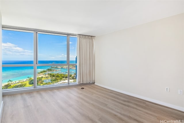 unfurnished room with a view of the beach, a water view, and light wood-type flooring