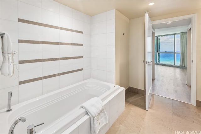 bathroom with a relaxing tiled tub, wood-type flooring, and a water view